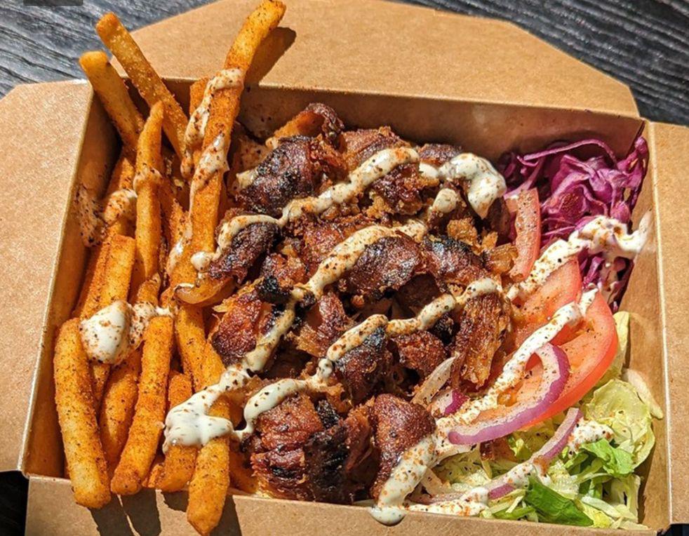 A döner box: shaved meat over fries with sauce and vegetables