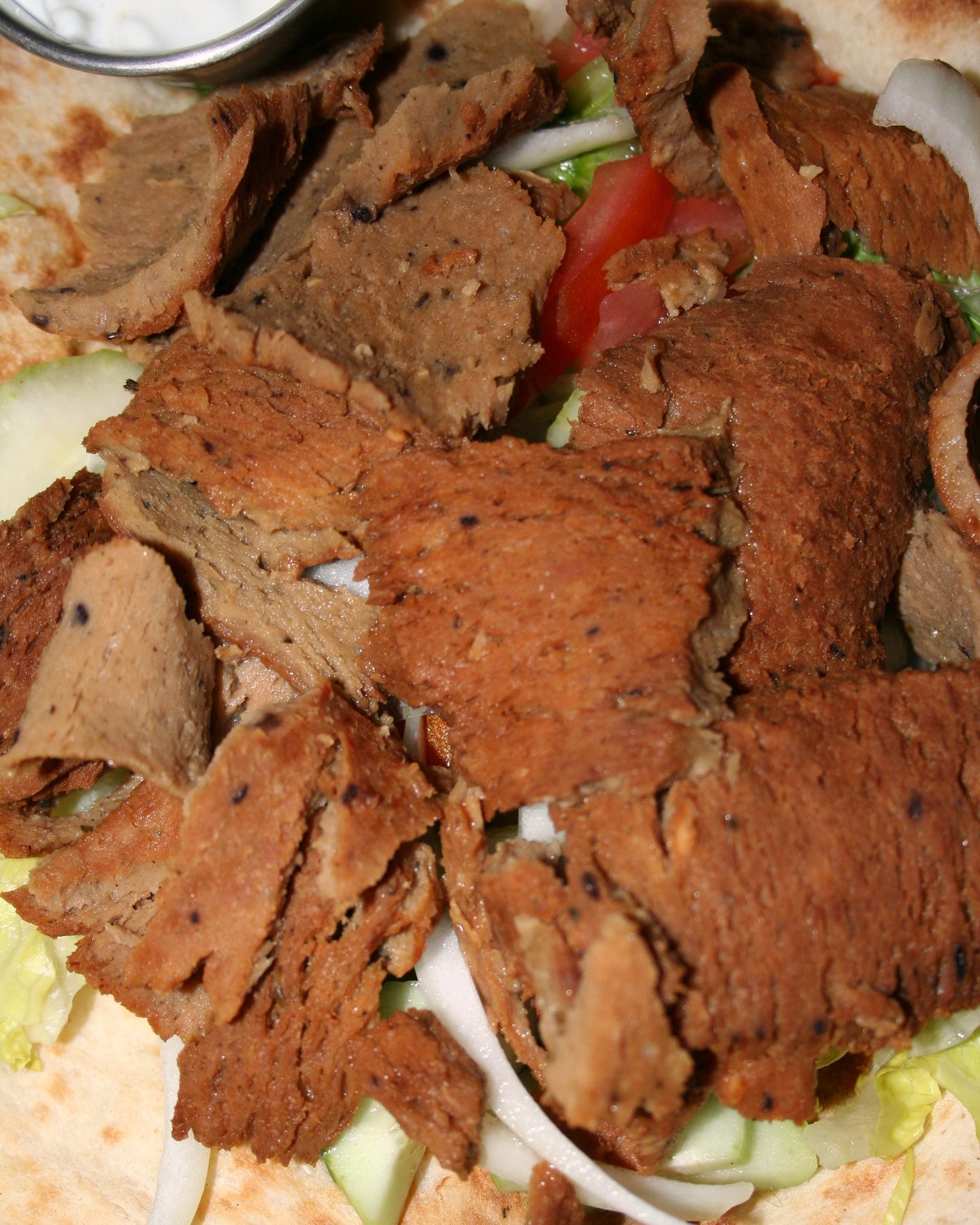 Sliced gyro meat, tomato, onion, cucumber, lettuce, pita, and tzatziki arranged on a plate
